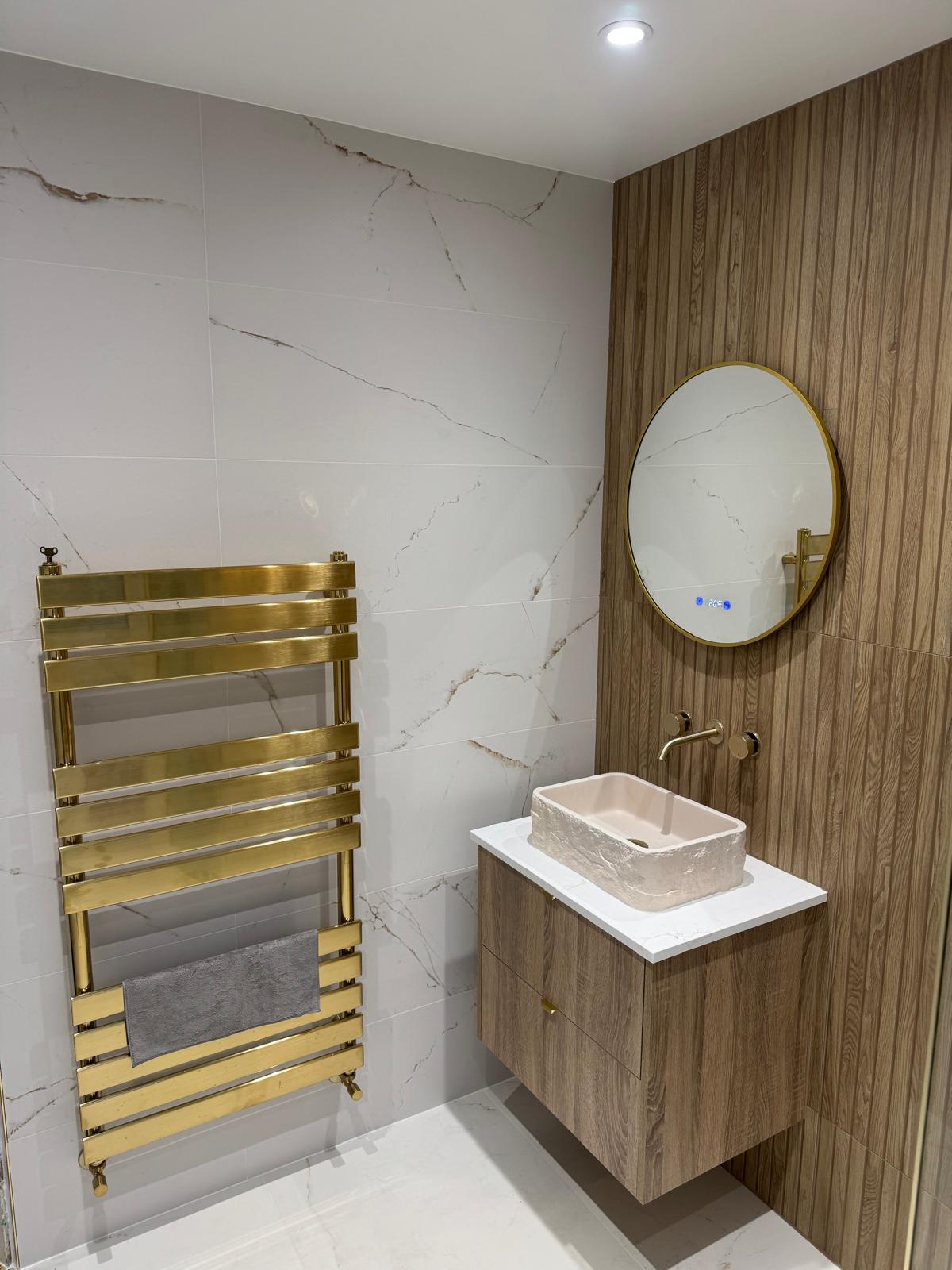 Luxury bathroom installation with floating vanity, gold towel radiator and illuminated mirror by MDS NE